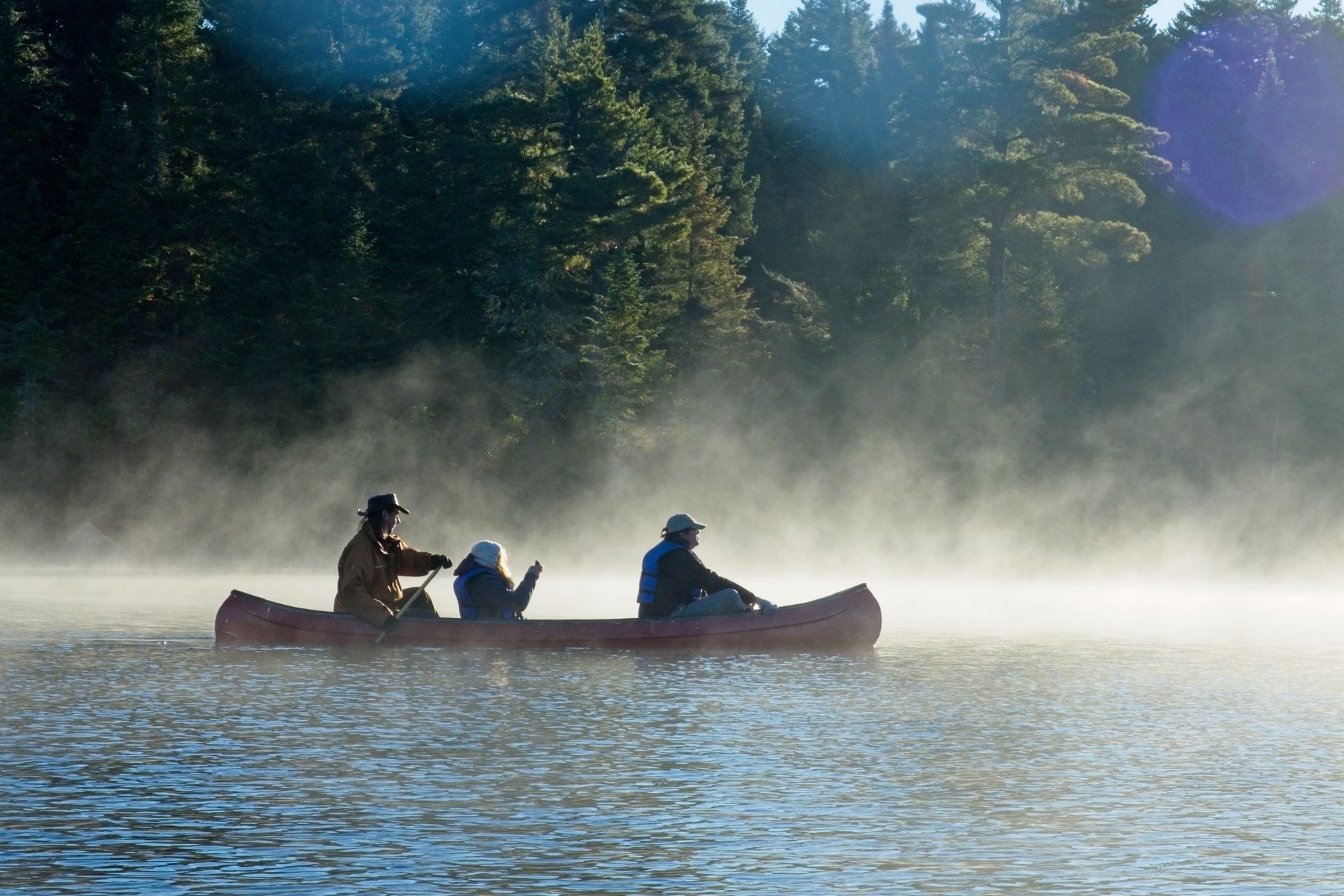 Un homme pousse à la perche une pirogue sur une large rivière le long d'îlots herbeux.